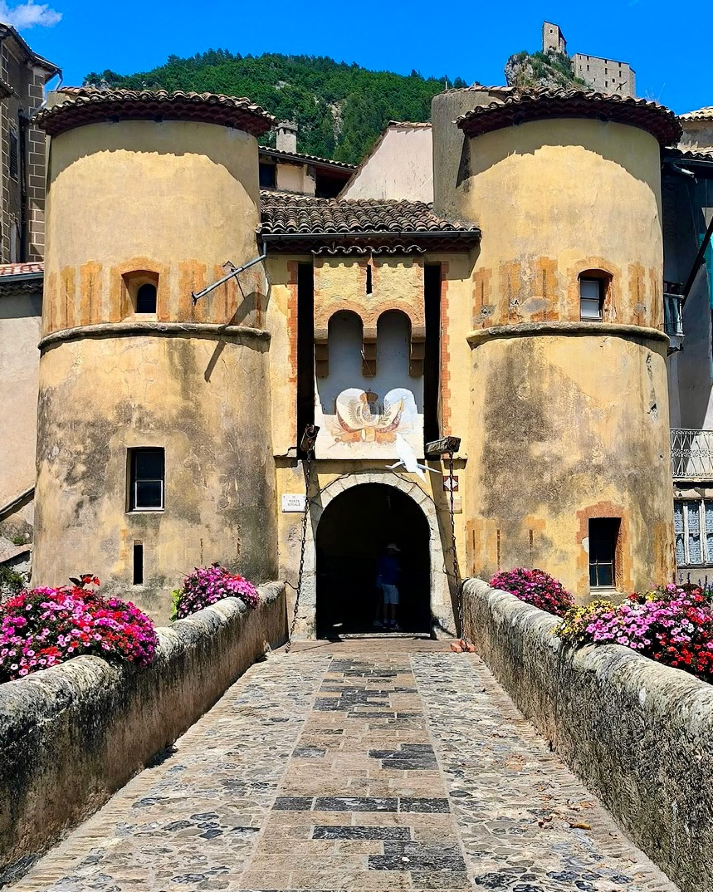 From the moment they arrive, visitors are greeted by an impressive drawbridge spanning the Var River. Once through the Royal Gate, they enter a true fortified town where cobbled streets wind between tall historic houses, vaulted passageways, shaded squares, façades in muted tones.